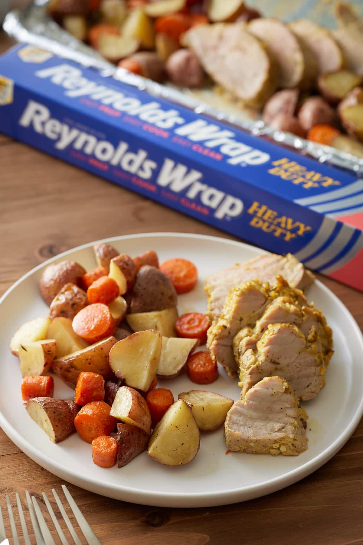 pork tenderloin with carrots and potatoes on white plate with foil paper in box in the background