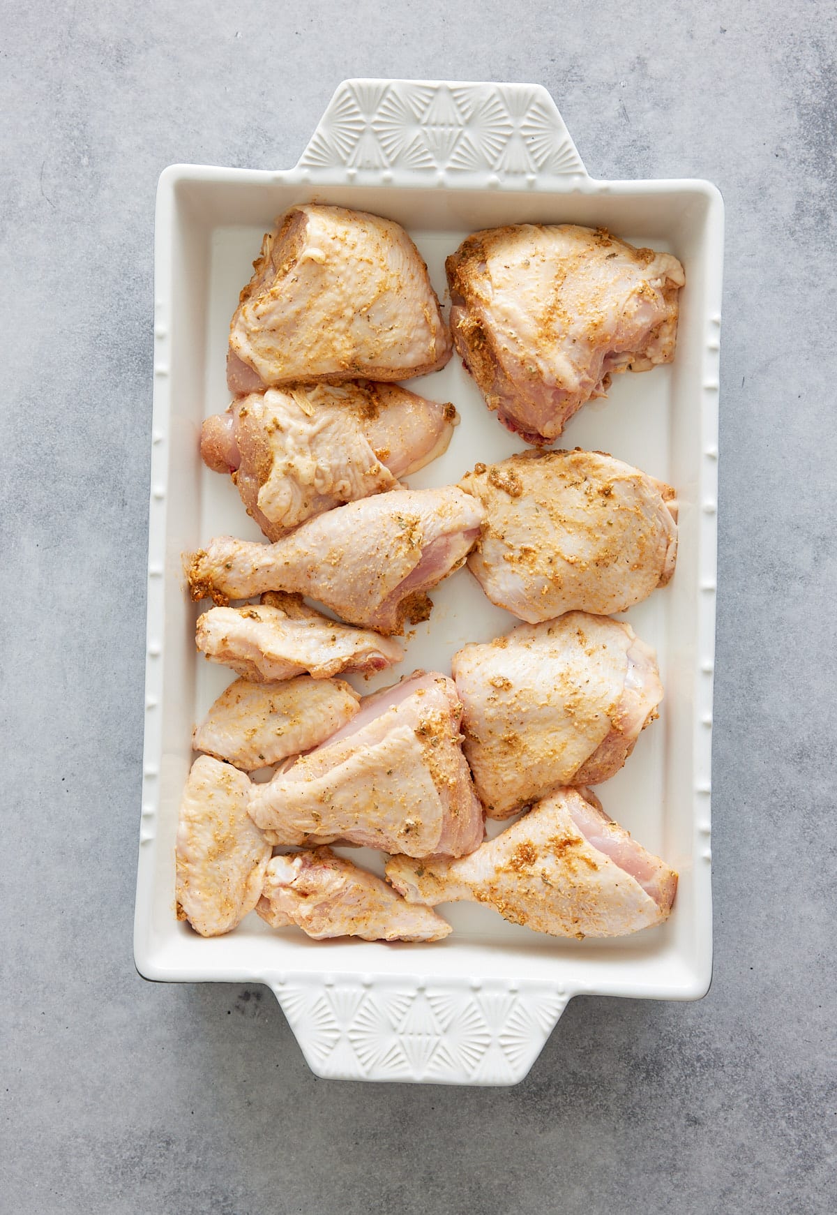 raw chicken pieces in a white baking dish