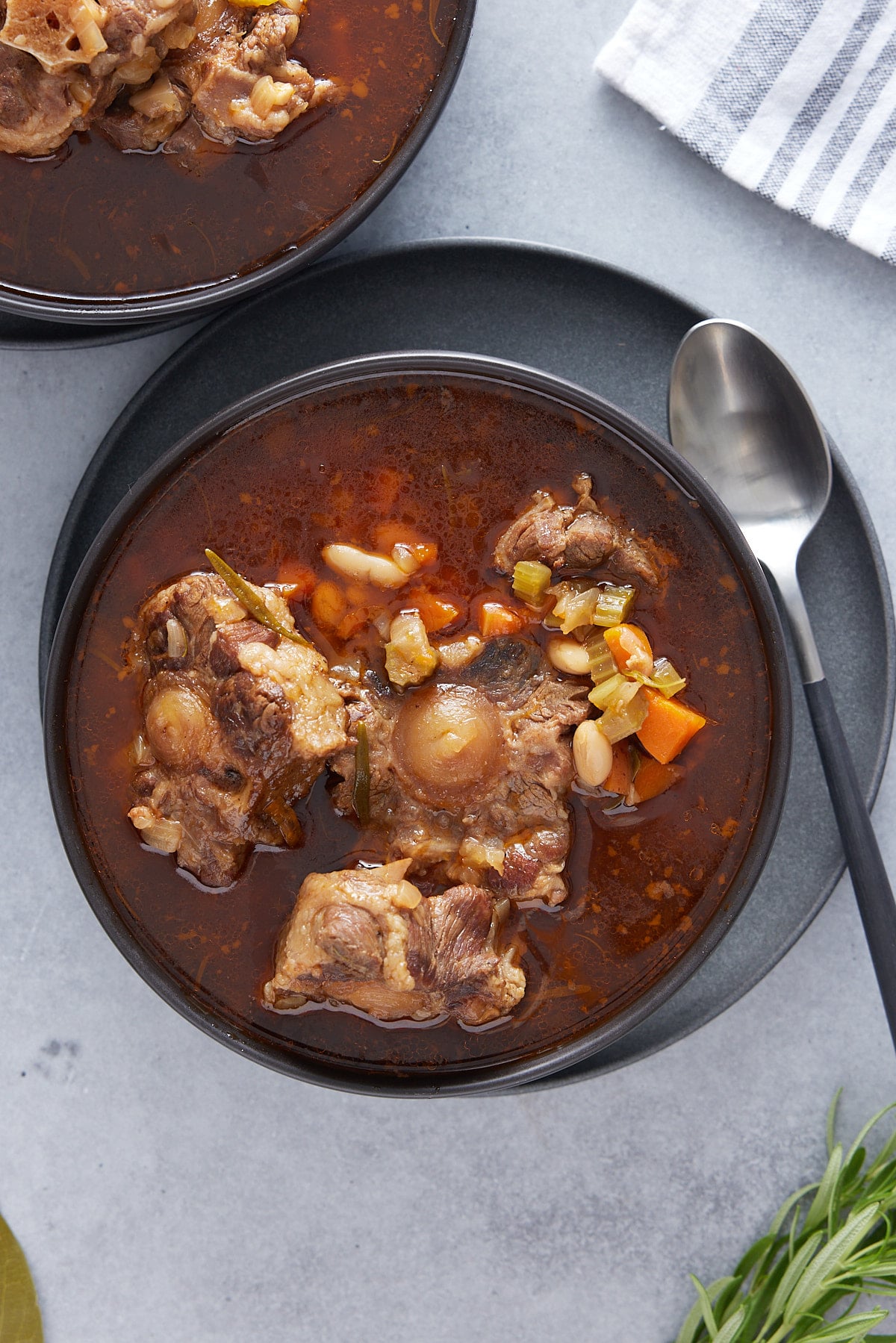 a bowl of oxtail stew next to a spoon on a gray plate