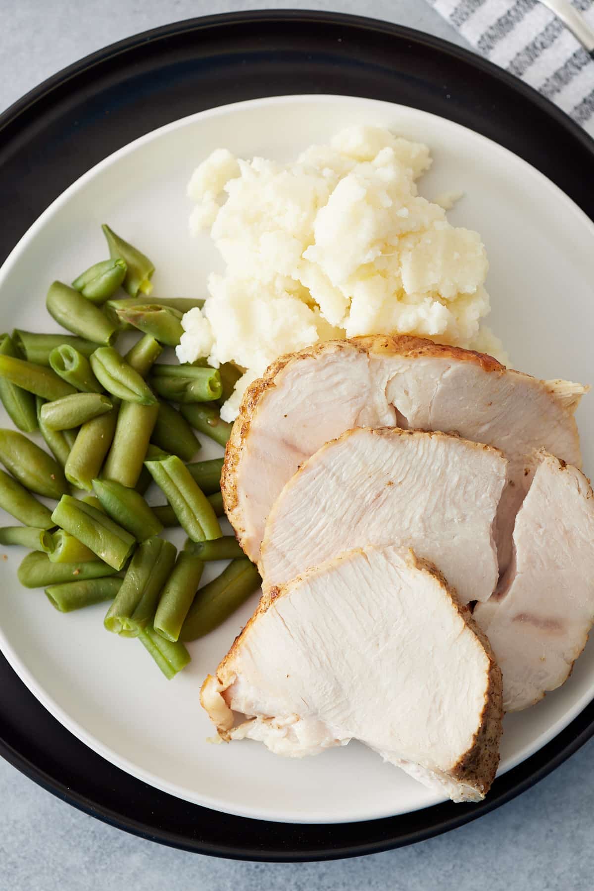 White plate with slices of turkey breast, mashed potato and green beans