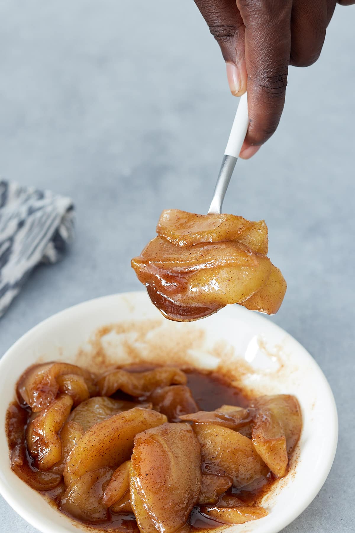 White bowl of fried apples and a hand holding a spoon of apples