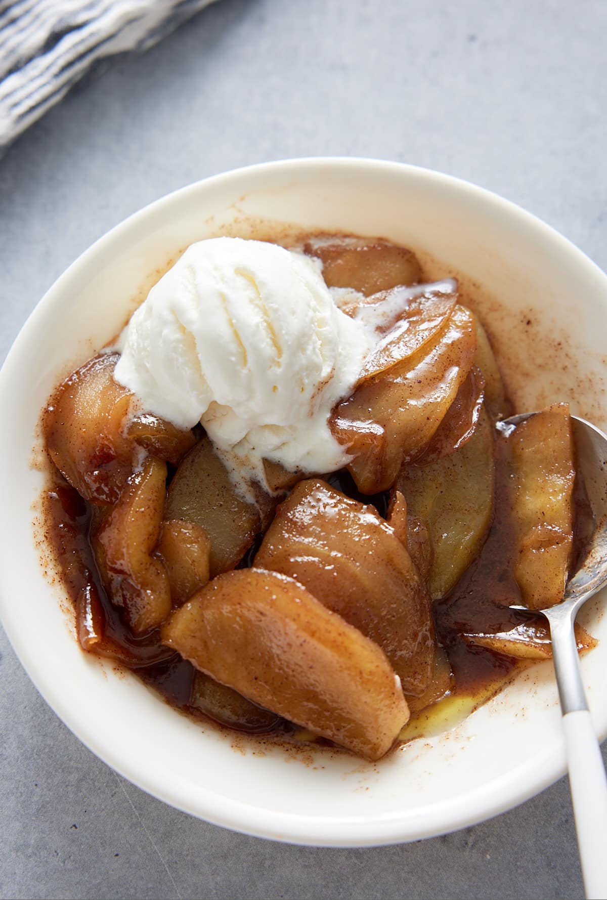 Southern fried apples in a white bowl with a scoop of ice cream and a dessert spoon