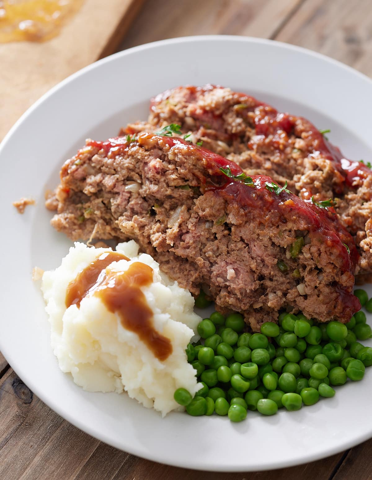 White plate with 2 slices of Southern meatloaf, mash potato, gravy and green peas.