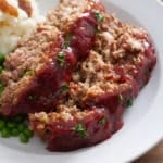 White plate with 2 slices of Southern meatloaf, mash potato, gravy and green peas.