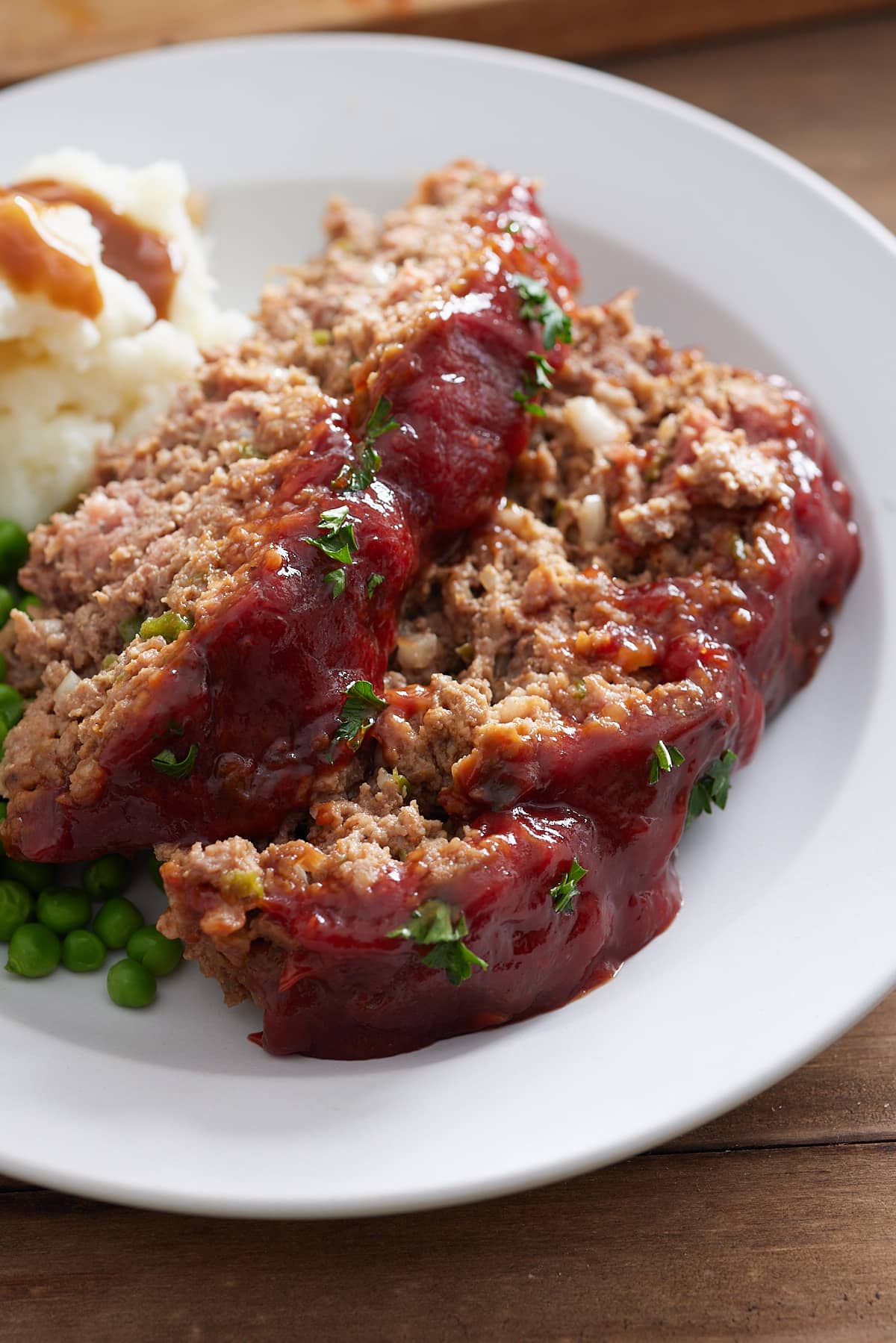 White plate with 2 slices of Southern meatloaf, mash potato, gravy and green peas.