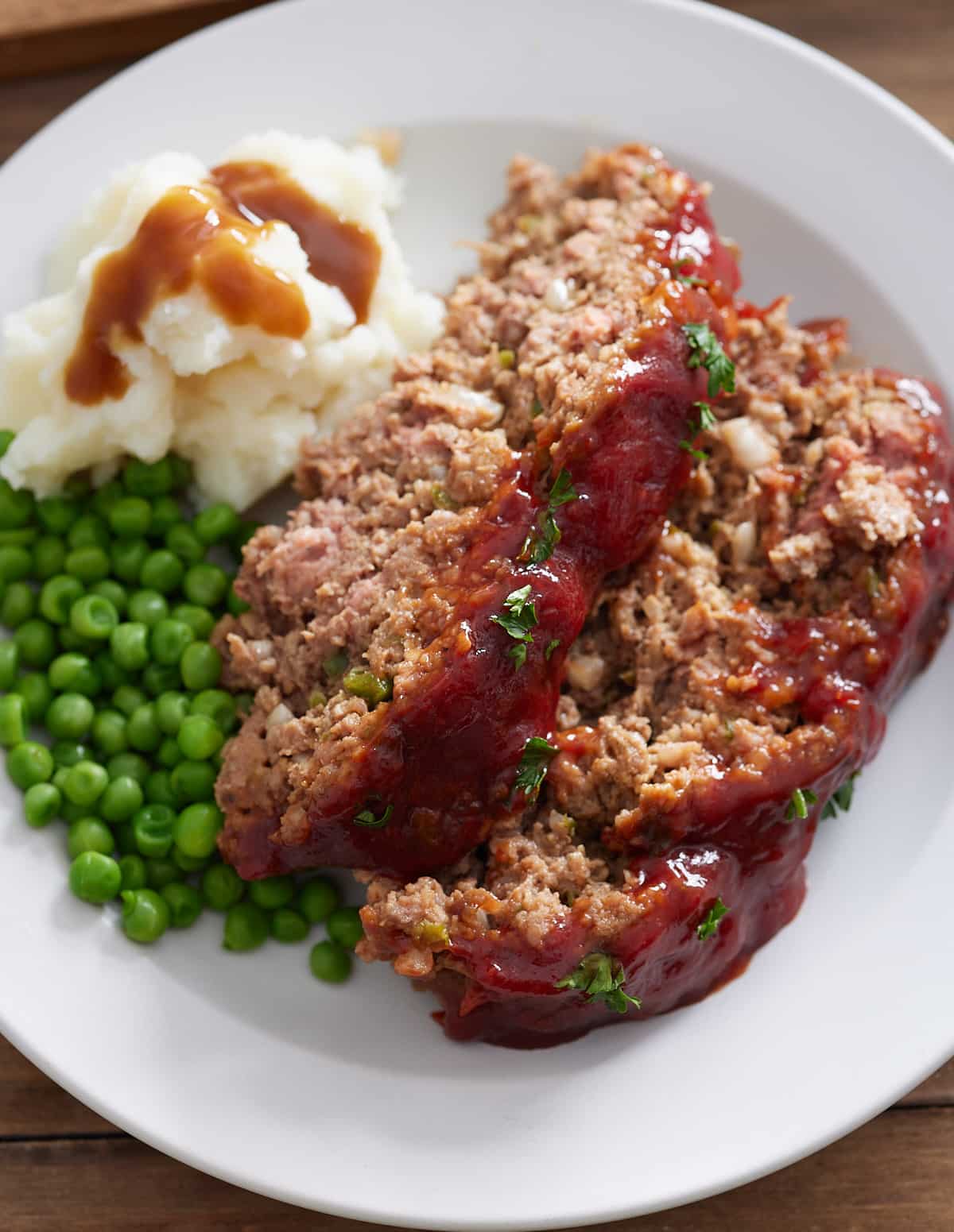 White plate with 2 slices of Southern meatloaf, mash potato, gravy and green peas.