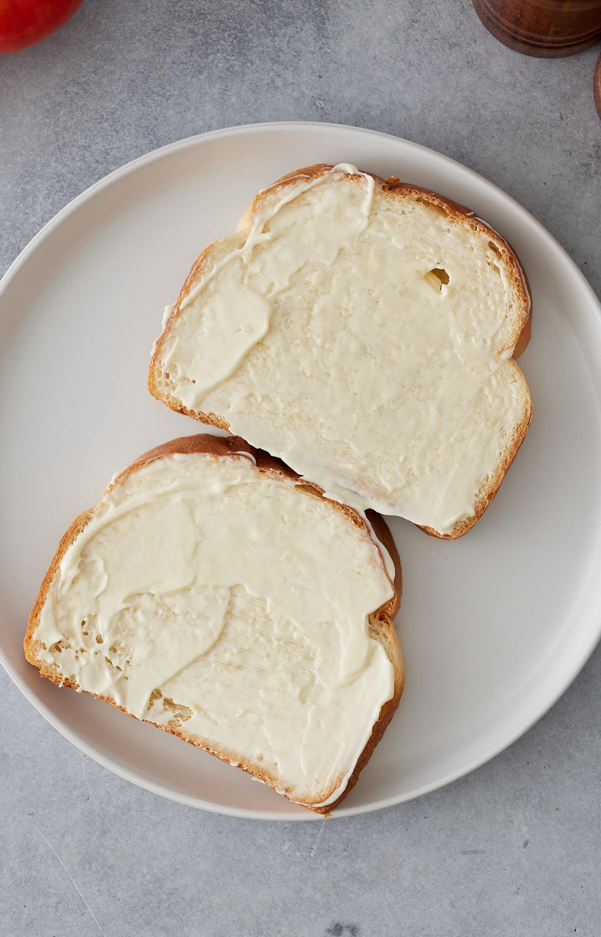 A white plate with two slices of sandwich bread, spread with mayonnaise