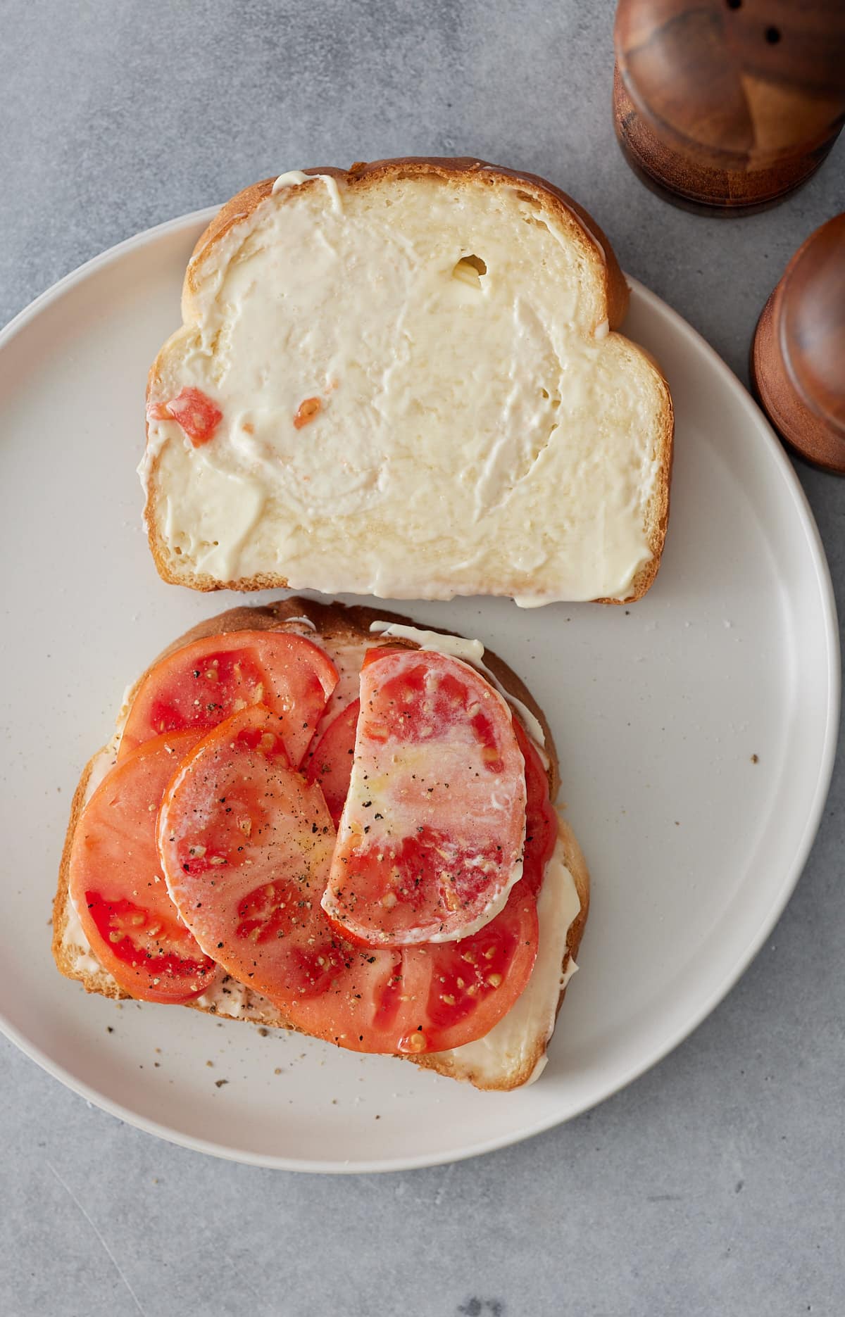 Top down image of white plate with 2 slices of sandwich bread spread with mayonnaise and sliced tomatoes on one half of the sandwich