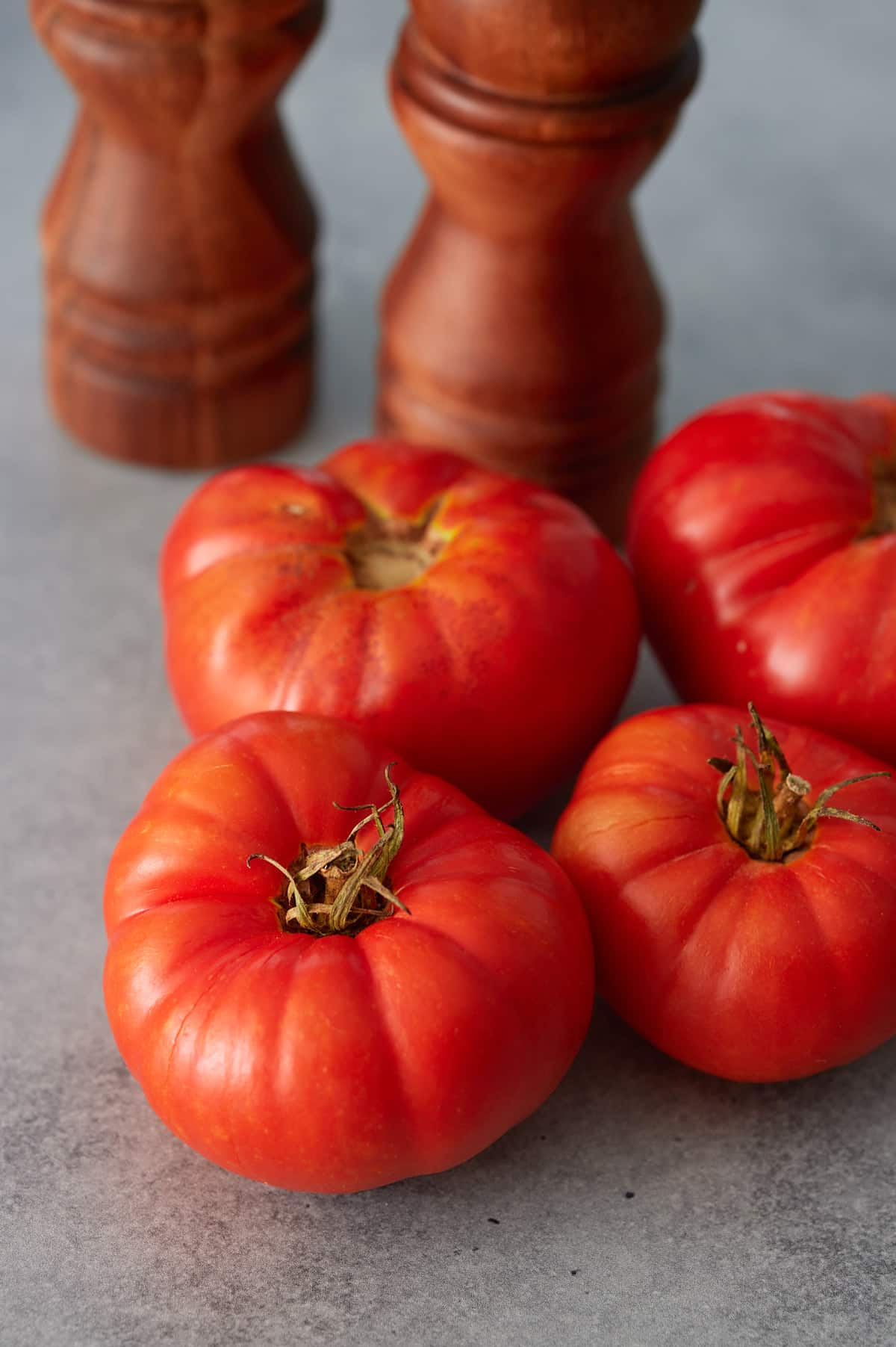 Four fresh heirloom tomatoes and salt and pepper grinders laid onto a marble surface