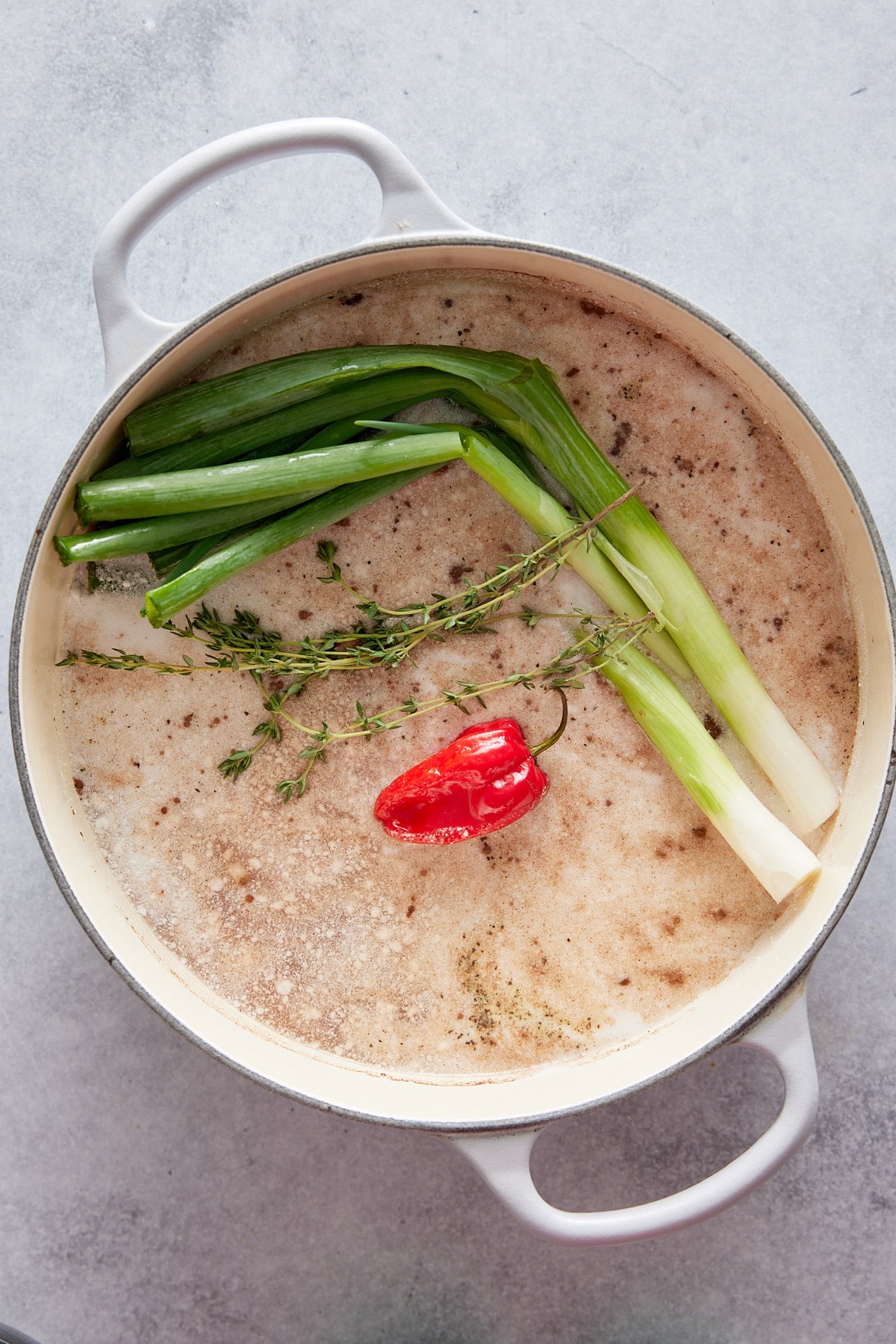 Dutch oven containing rice, stock, fresh green onions, sprigs or thyme and a Scotch bonnet