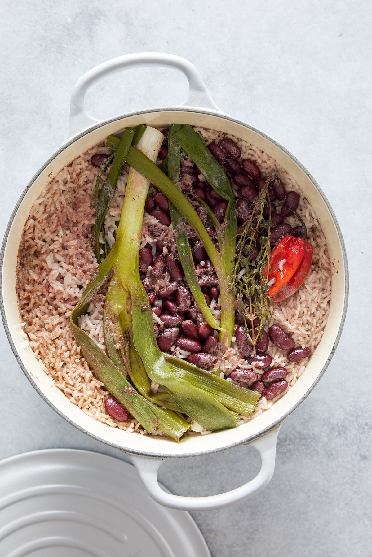 Dutch oven containing cooked rice, peas, fresh green onions, sprigs or thyme and a Scotch bonnet