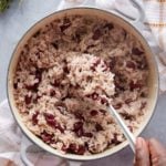 Dutch oven containing cooked Jamaican rice and peas and a hand with a serving spoon of rice