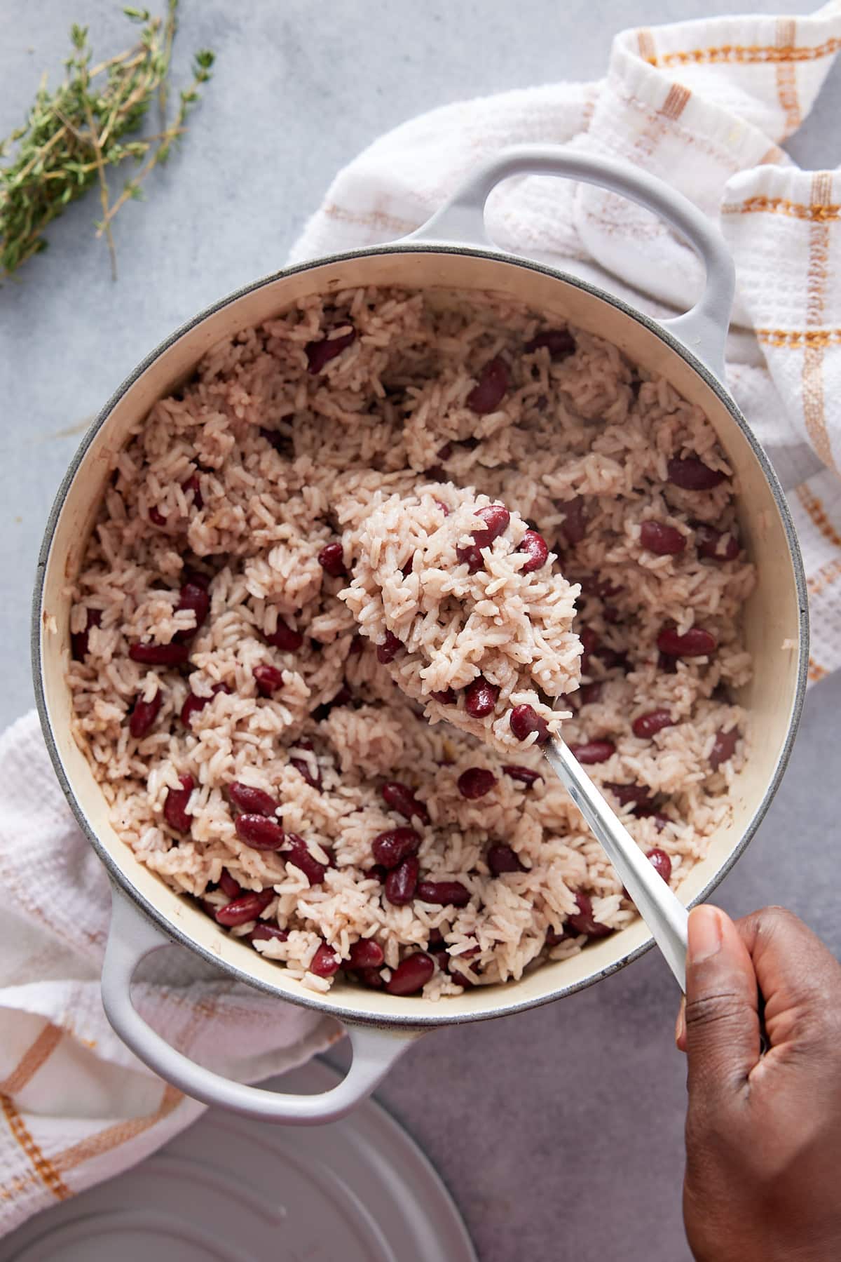 Dutch oven containing cooked Jamaican rice and peas and a hand with a serving spoon of rice