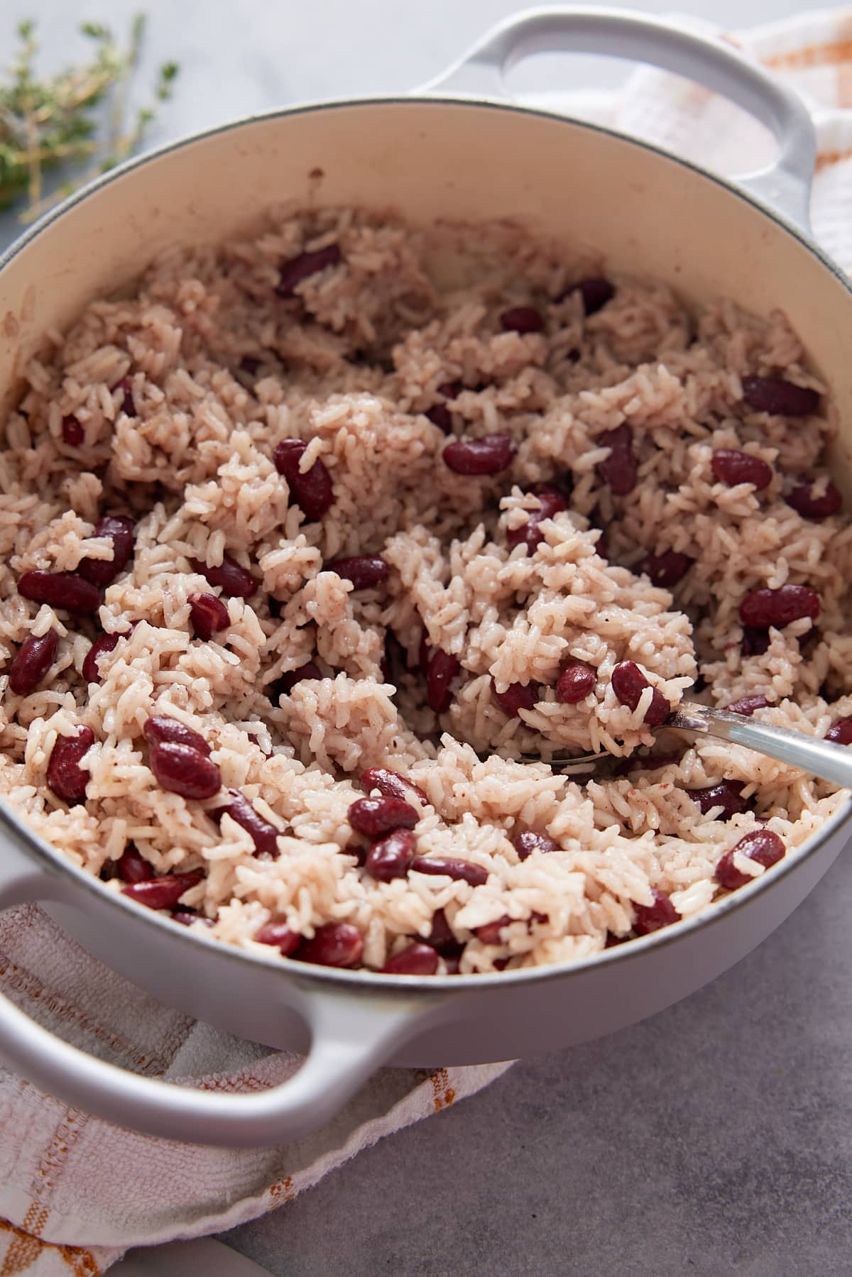 Dutch oven containing cooked Jamaican rice and peas and a serving spoon