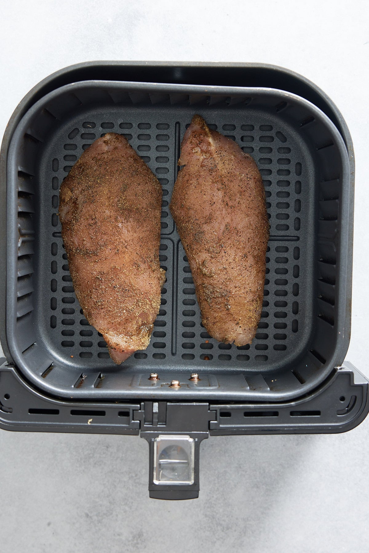 Uncooked, seasoned turkey tenderloins set into air fryer basket