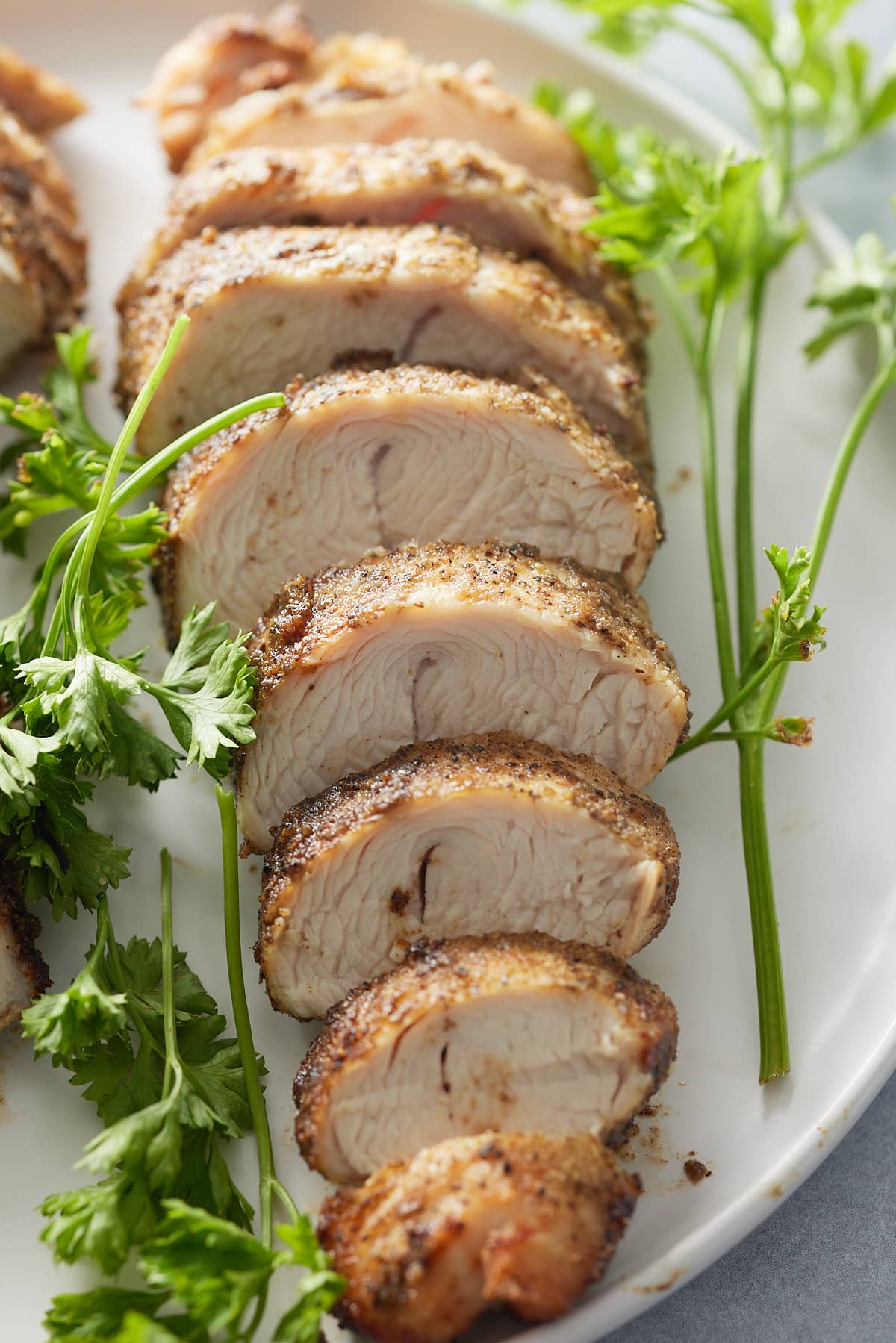 Cooked and sliced turkey tenderloin set onto white plate with garnish of fresh parsley sprigs