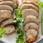 Two sliced turkey tenderloins set onto a white serving platter with a garnish of fresh parsley