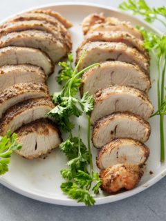 Two sliced turkey tenderloins set onto a white serving platter with a garnish of fresh parsley