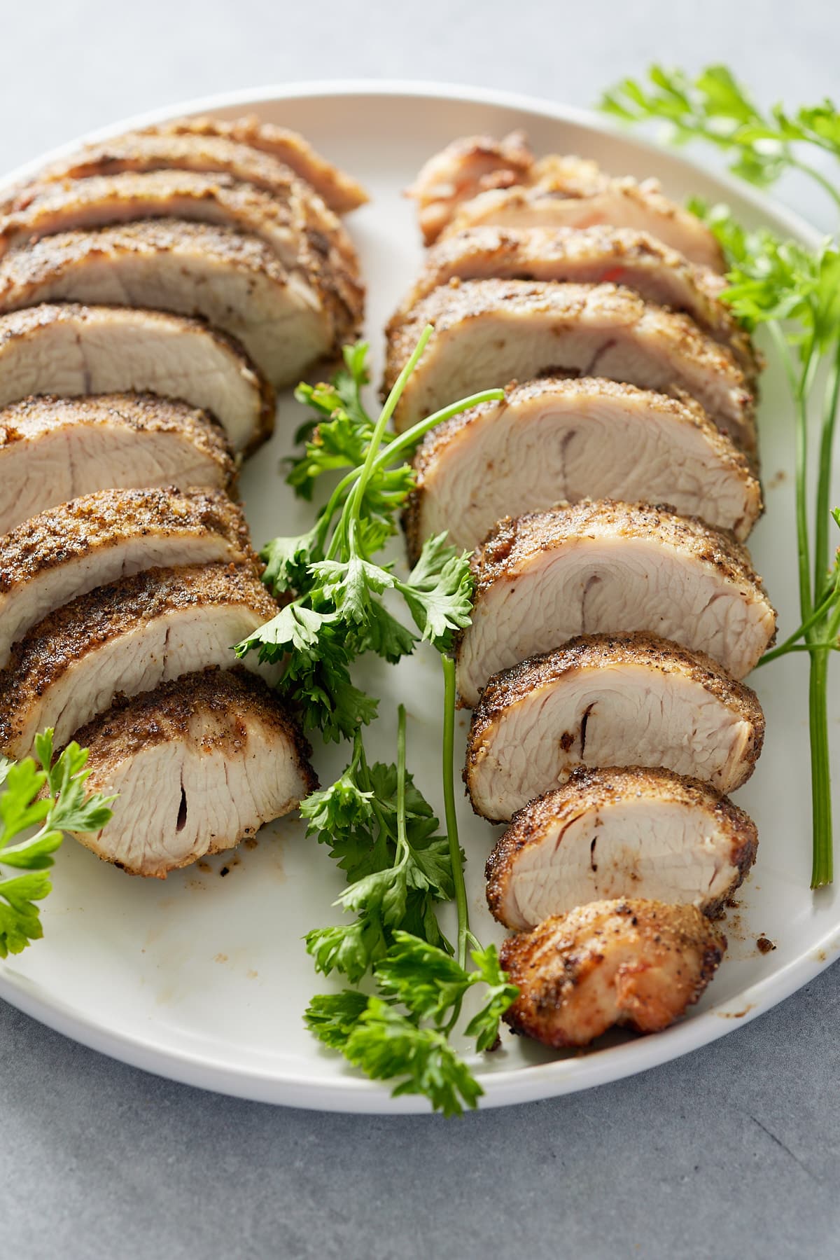 Two sliced turkey tenderloins set onto a white serving platter with a garnish of fresh parsley