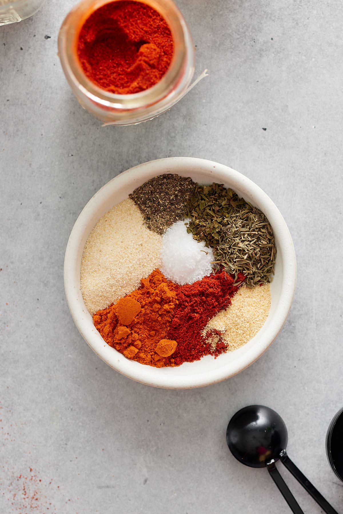 White bowl containing ingredients for blackened seasoning and an open jar of smoked paprika