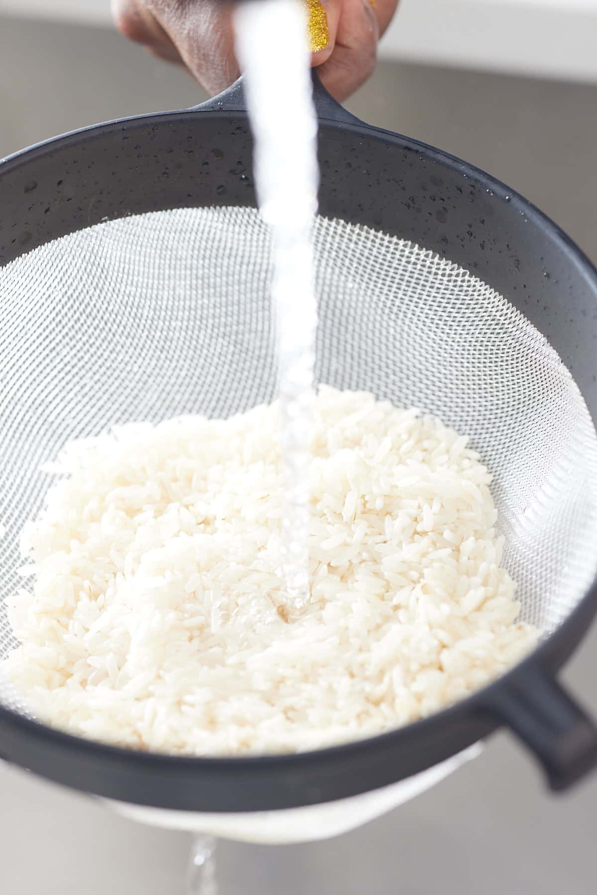 rinsing raw rice in a mesh strainer