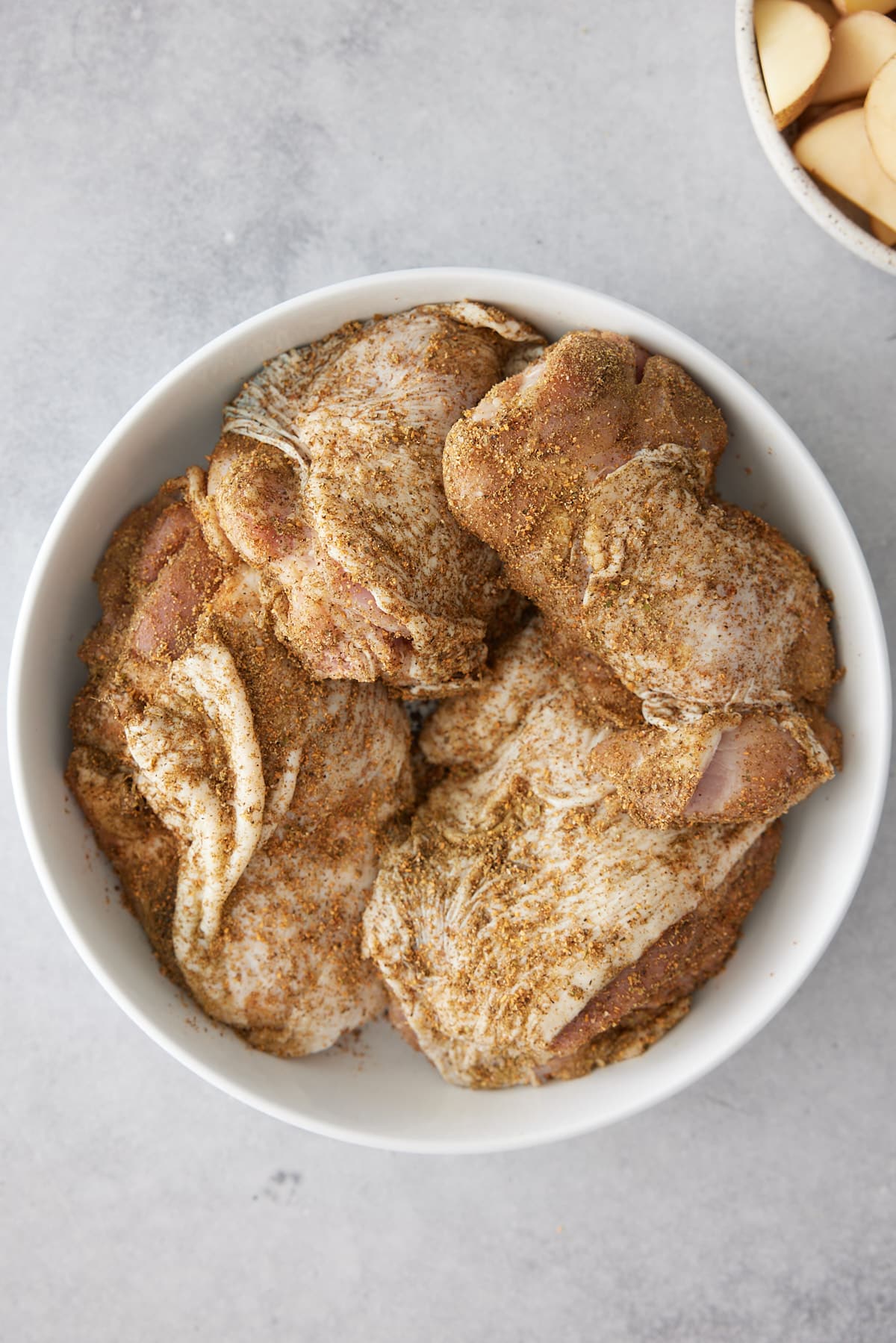 Skin on turkey thighs coated in spice rub set into a white bowl