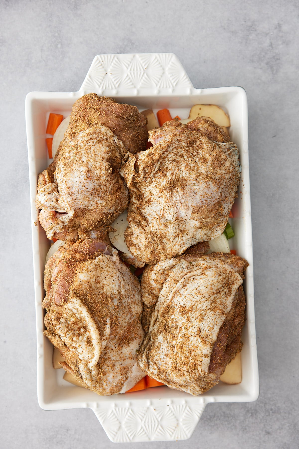 White oven proof dish with a layer of vegetables and seasoned turkey thighs set on top