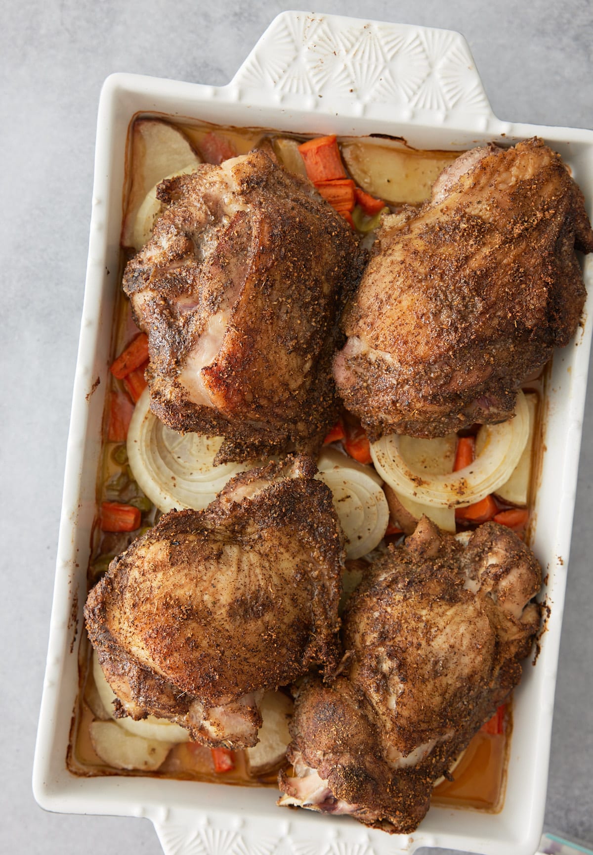 White oven proof dish with a layer of cooked vegetables and oven baked turkey thighs set on top