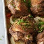 Close up image of white oven proof dish with a layer of cooked vegetables and oven baked turkey thighs set on top