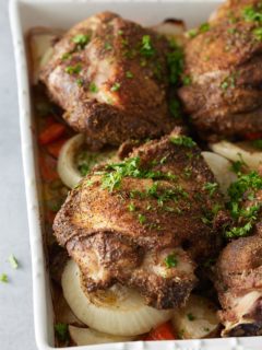 Close up image of white oven proof dish with a layer of cooked vegetables and oven baked turkey thighs set on top