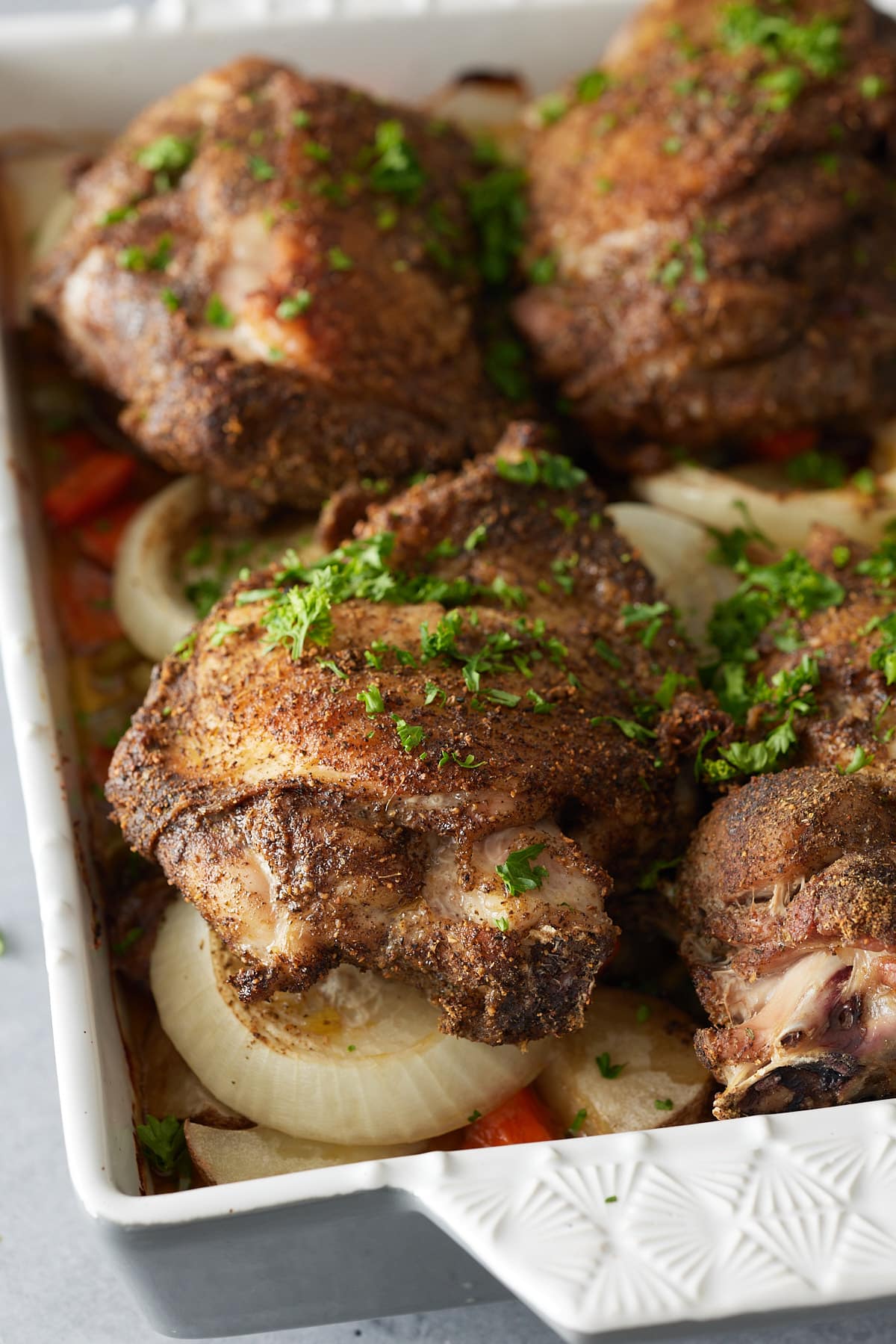 Close up image of white oven proof dish with a layer of cooked vegetables and oven baked turkey thighs set on top