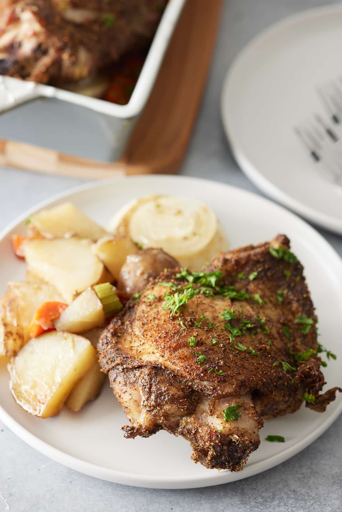 White plate with oven baked turkey thighs, garnished with fresh parsley and served with a side of vegetables