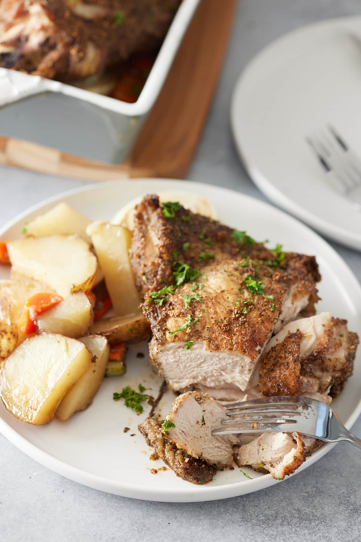 White plate with sliced oven baked turkey thighs, garnished with fresh parsley and served with a side of vegetables