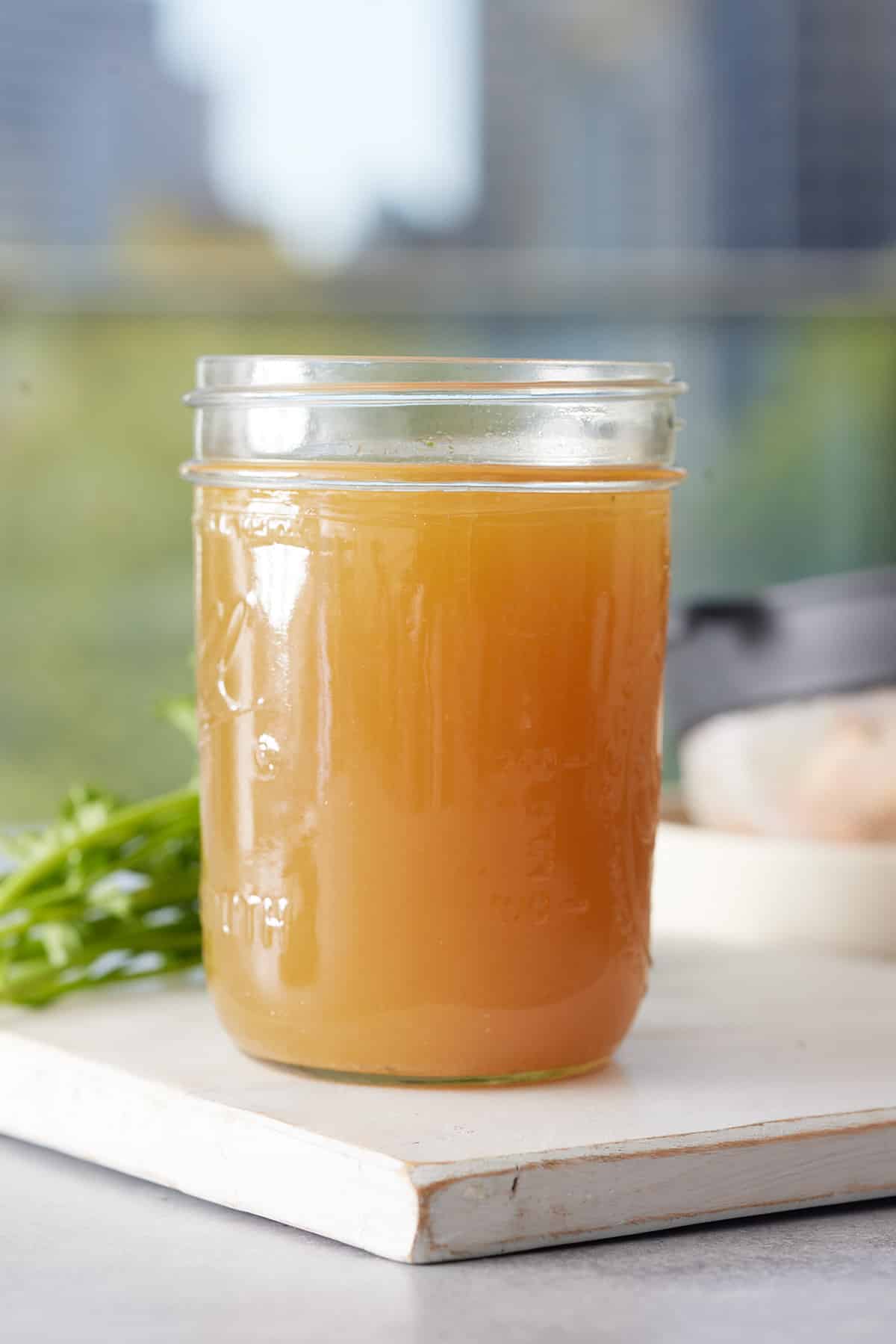 Jar of shrimp stock set on a wooden board to cool