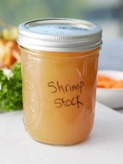 Lidded jar of shrimp stock with label set onto a wooden board