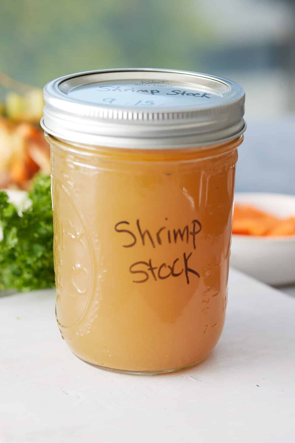 Lidded jar of shrimp stock with label set onto a wooden board