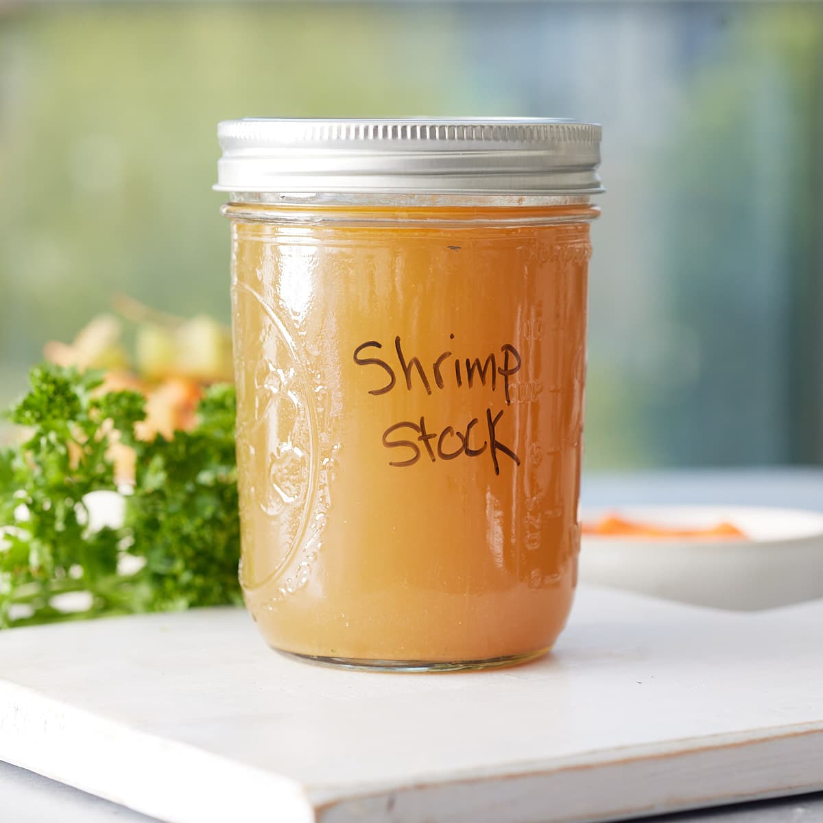 Lidded jar of shrimp stock with label set onto a wooden board