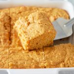 Close up image of slice of sweet potato cornbread being cut from dish