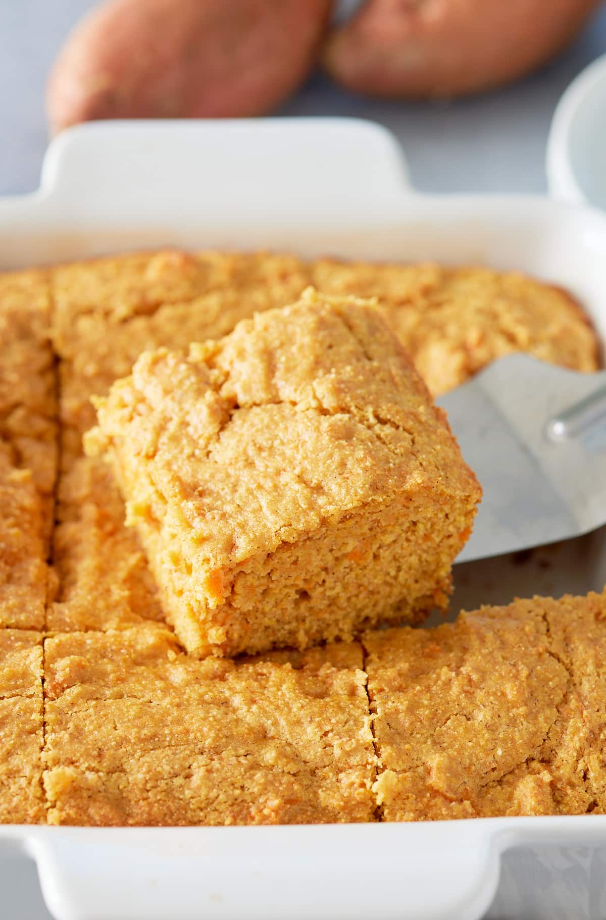 Close up image of slice of sweet potato cornbread being cut from dish