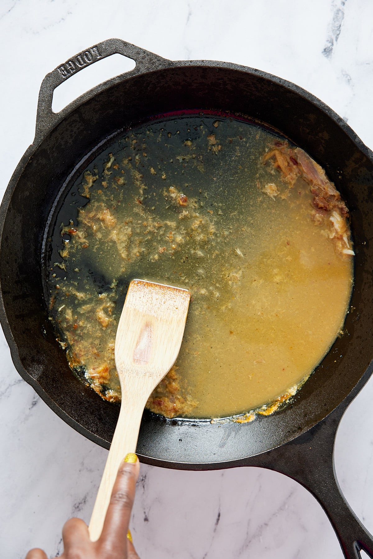 De-glazing cast iron skillet with water and turkey pieces being scraped up using a wooden spatula