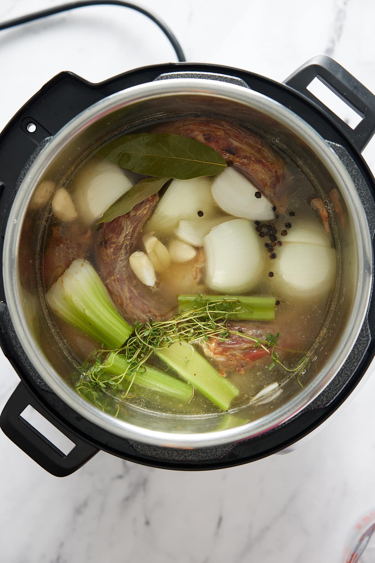 Pressure cooker pot containing turkey pieces, raw vegetables, herbs, spices and water
