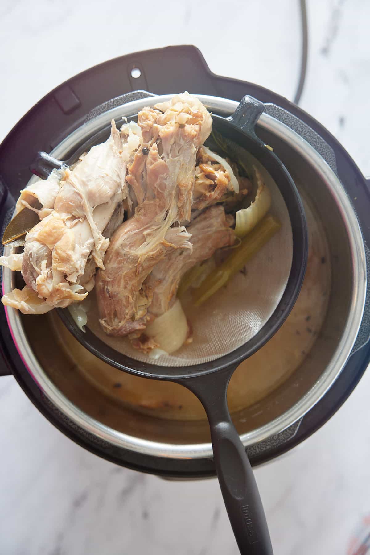 Sieve filled with cooked turkey pieces and vegetables ready for discarding