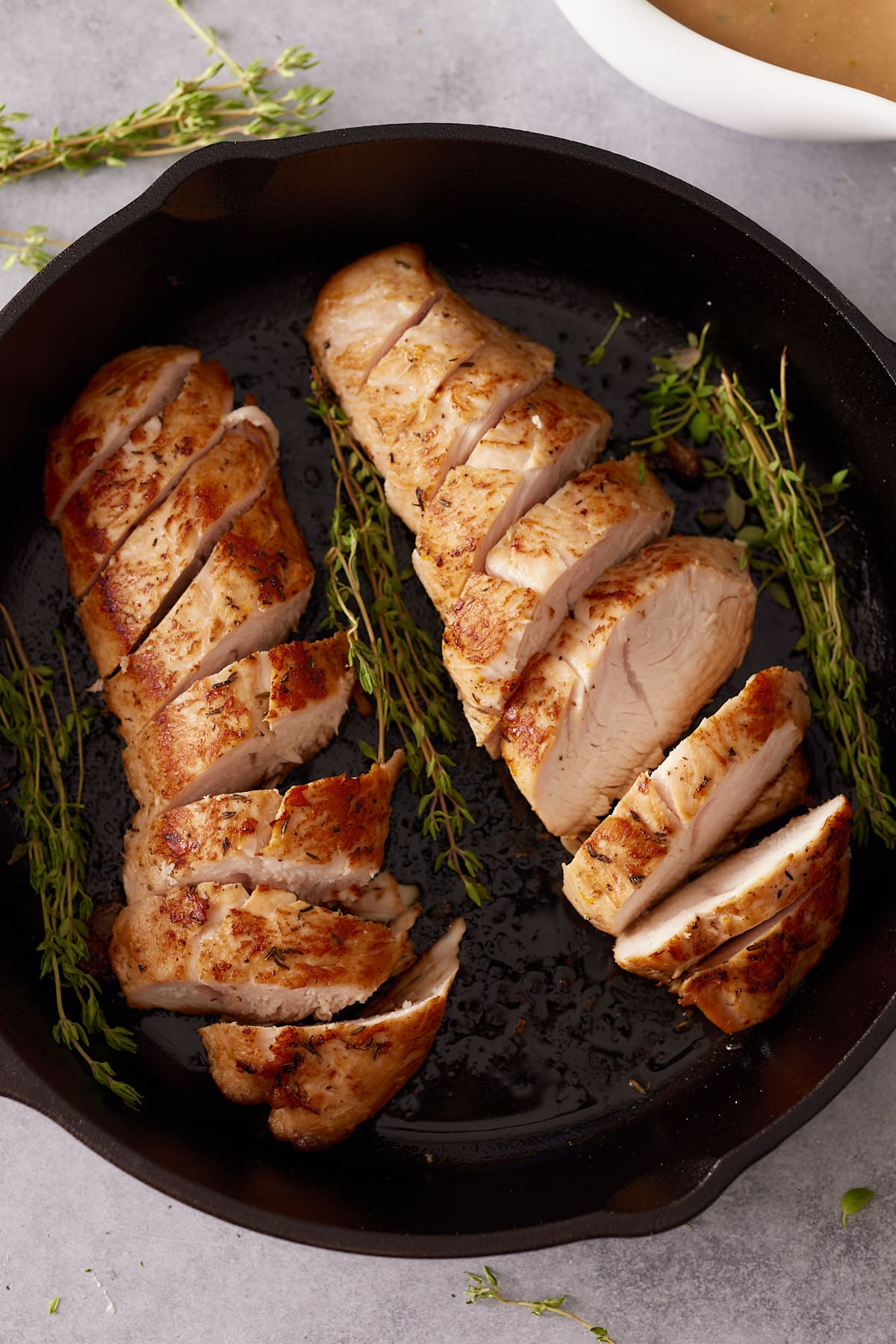 Top down image of cast iron skillet containing two cooked and sliced turkey tenderloins and sprigs of fresh thyme
