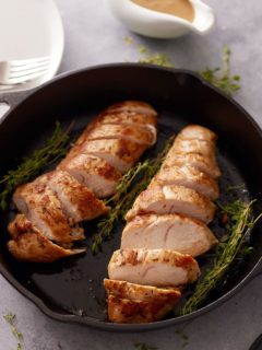 Cast iron skillet containing two cooked and sliced turkey tenderloins and sprigs of fresh thyme and just of gravy set alongside