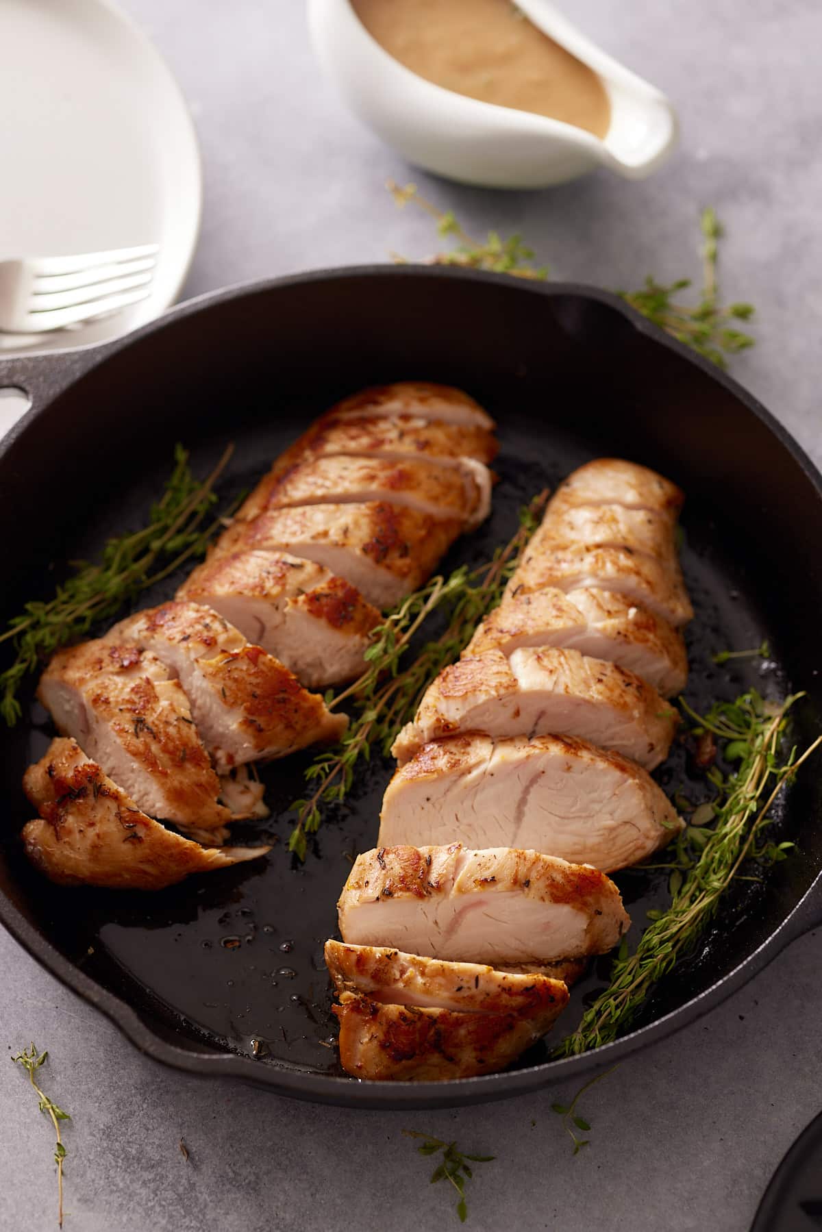 Cast iron skillet containing two cooked and sliced turkey tenderloins and sprigs of fresh thyme and just of gravy set alongside