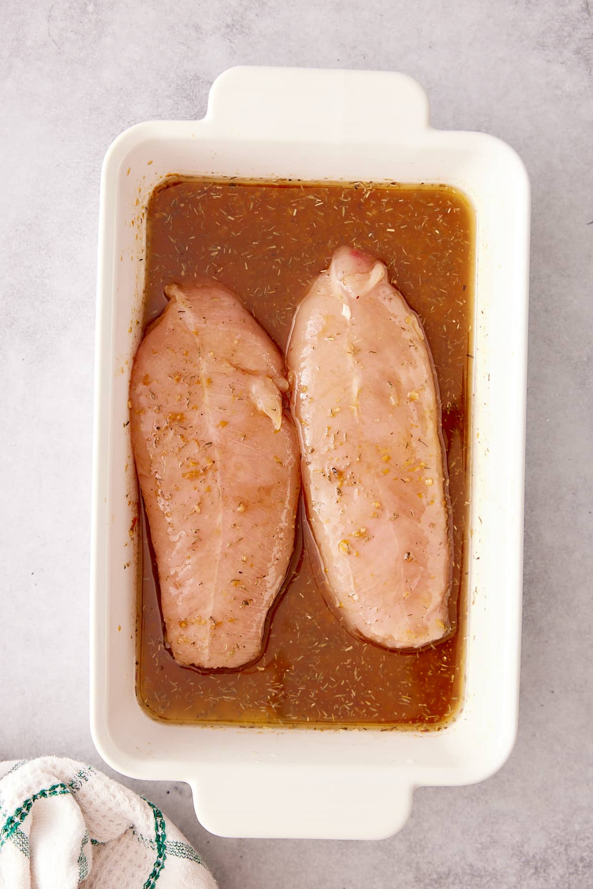 White dish containing two turkey tenderloins covered in marinade