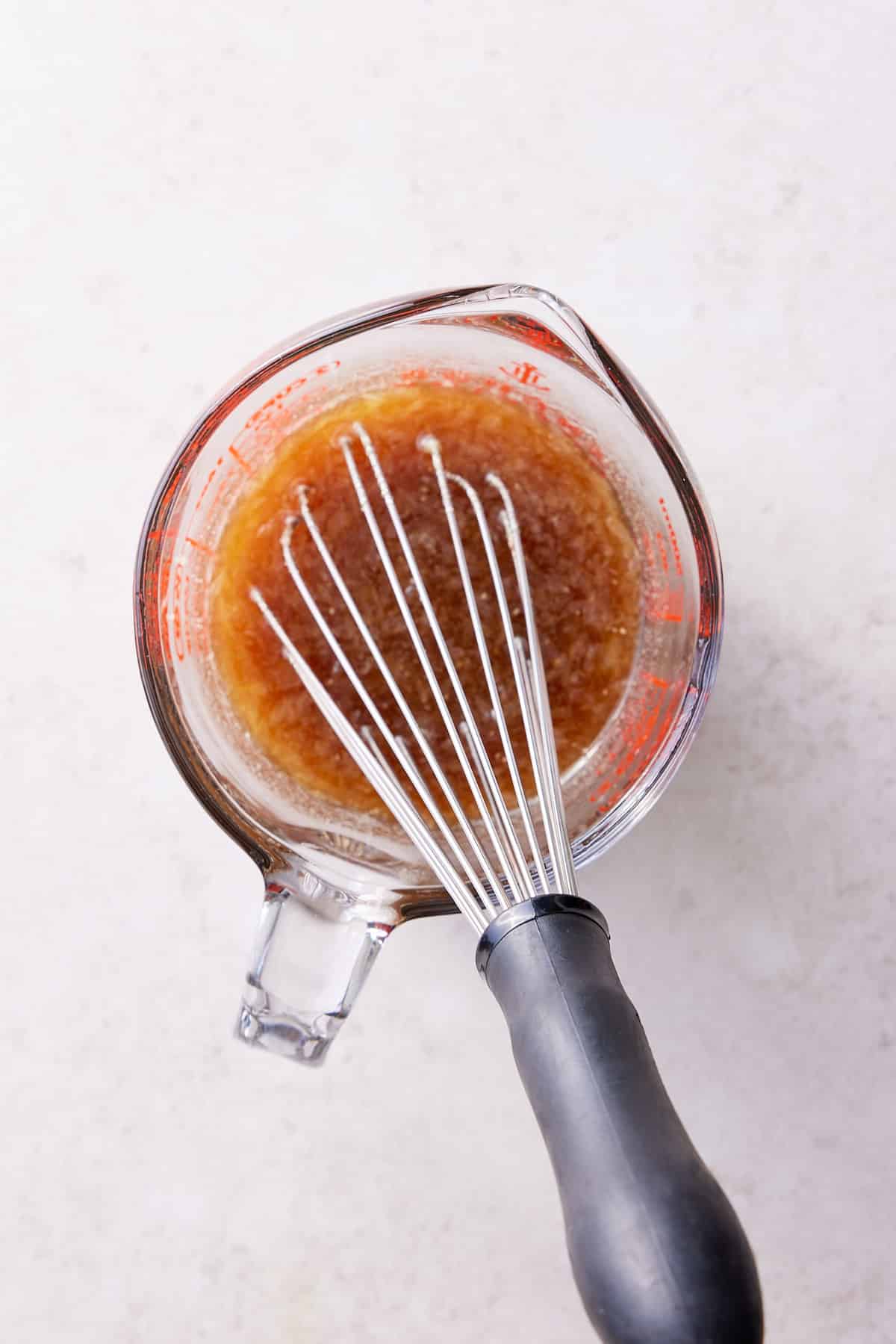 Glass measuring jug filled with lime juice, brown sugar and a balloon whisk