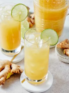 Two glasses decorated with slices of fresh lime filled with Jamaican ginger beer and a pitcher of Jamaican ginger beer set alongside