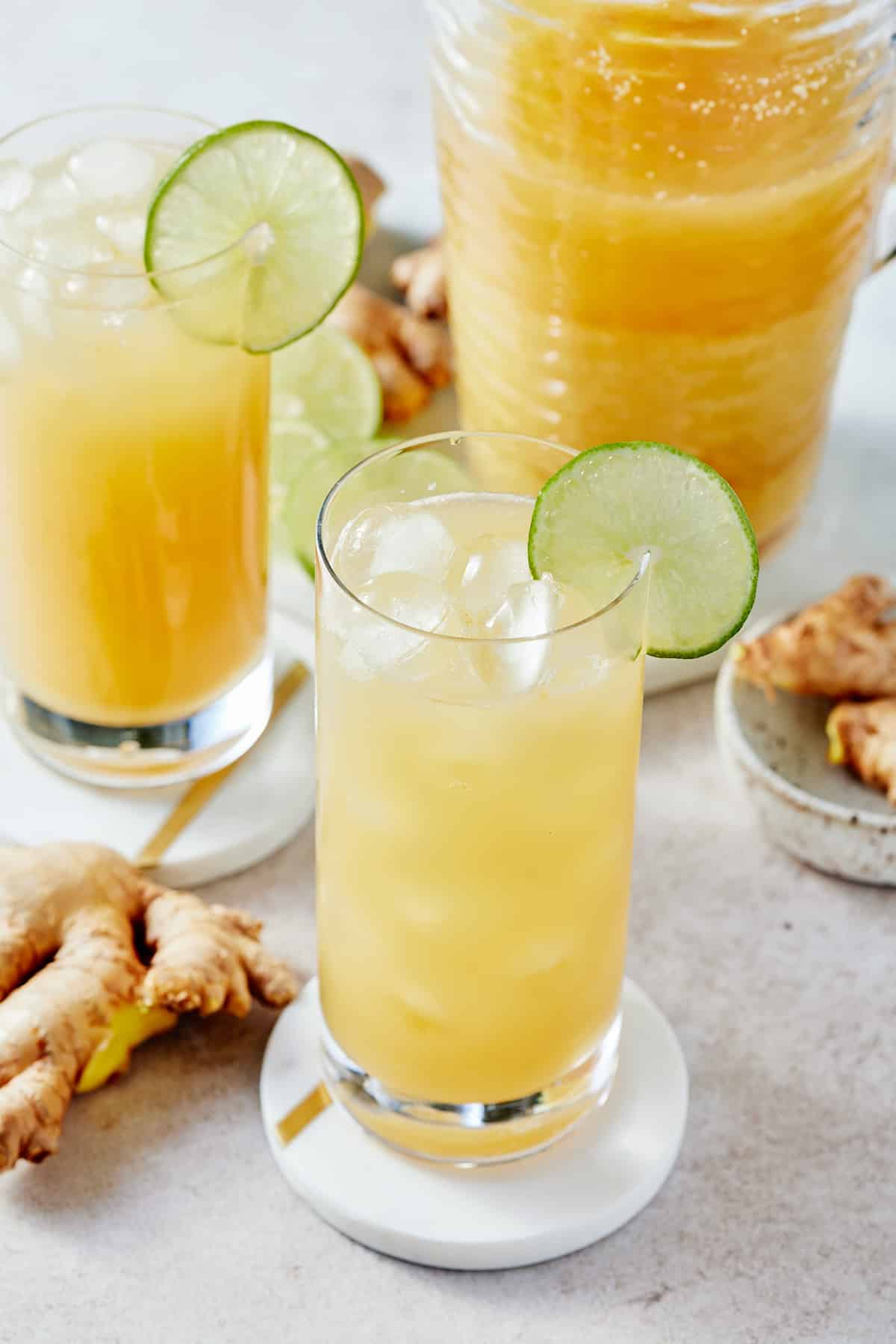 Two glasses decorated with slices of fresh lime filled with Jamaican ginger beer and a pitcher of Jamaican ginger beer set alongside