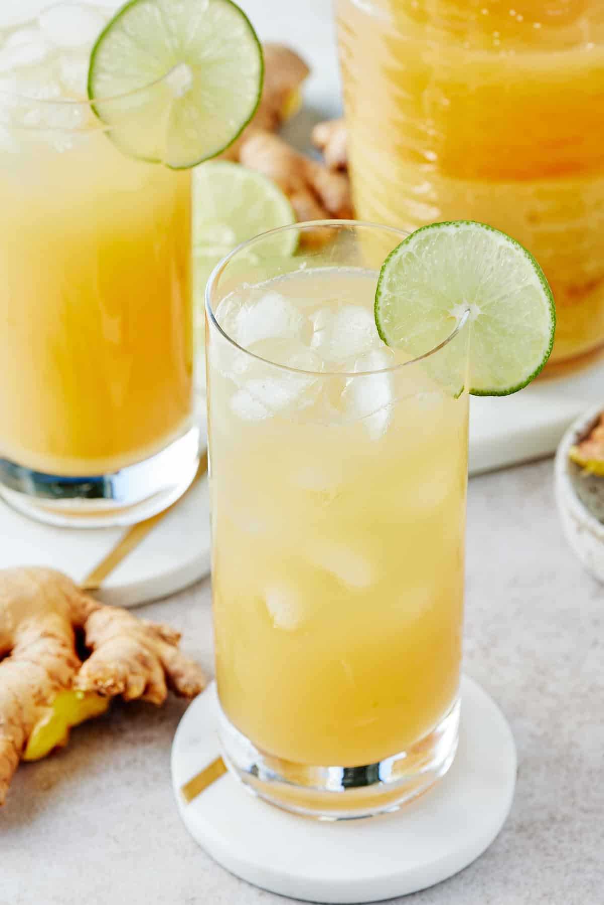 Two glasses decorated with slices of fresh lime filled with Jamaican ginger beer and a pitcher of Jamaican ginger beer set alongside
